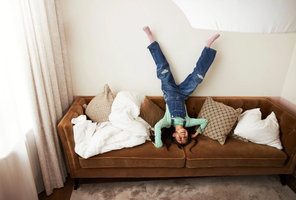 Flicka som står på huvudet i en soffa på ett hotellrum