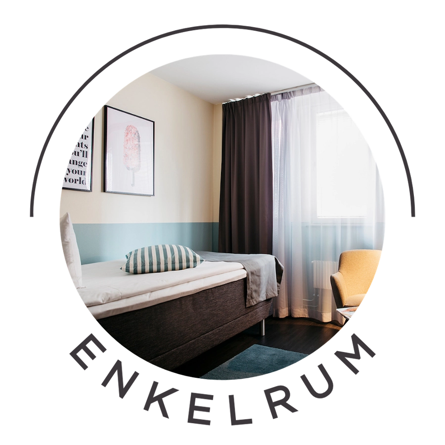 Bilden visar ett enkelrum på Kom Hotel. Rummet har ett fönster, en enkelsäng, skrivbord och en fåtölj med ett litet bord. Det sitter en tv på väggen och fönstret ramas in av gardiner. På väggen sitter två tavlor. Väggarna går i neutrala färger. 