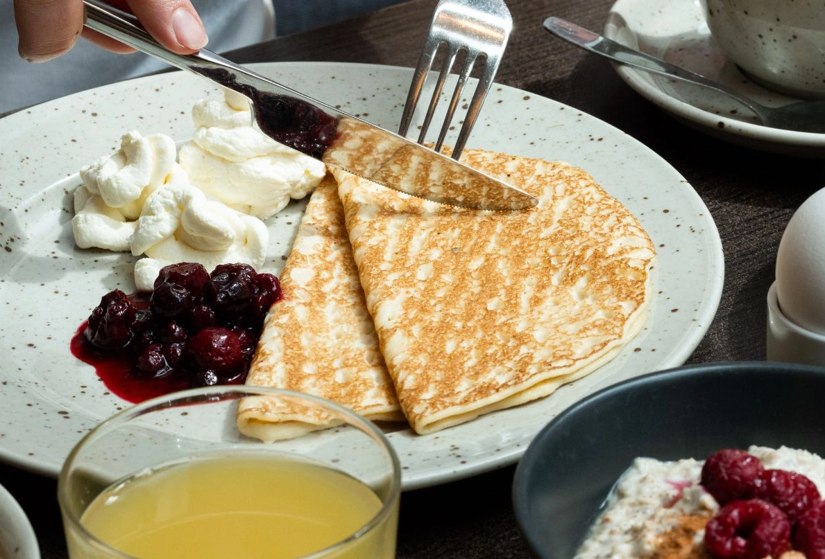 Tallrik med hotellfrukost - denna gång pannkakor med bärkompott och grädde. Ett glas juice och youghurt med bär syns i bilden.