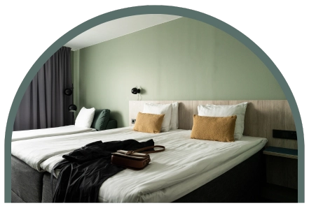 En bäddad säng i ett hotellrum. Bredvid står en bäddsoffa och festliga kläder ligger slängda på sängen. 