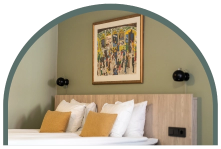 Bilden visar en hotellsäng med gavel i trä, gröna väggar och gula kuddar.