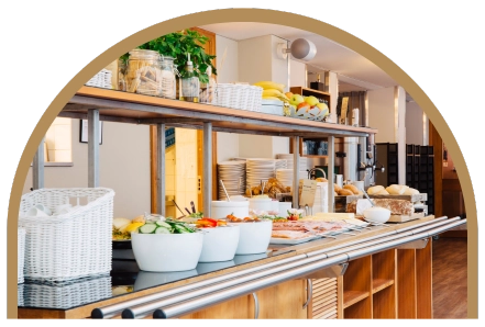 Frukostbuffébord i trä på Kom Hotel. Bordet är överfyllt av en uppdukad frukostbuffé med grönsaker, frukt och pålägg till smörgåsar.