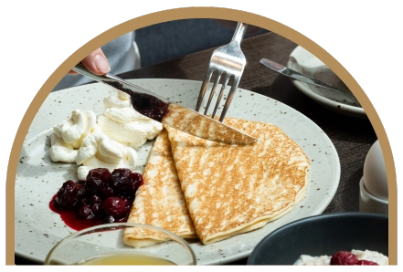 Tallrik med hotellfrukost - denna gång pannkakor med bärkompott och grädde. Ett glas juice och youghurt med bär syns i bilden.