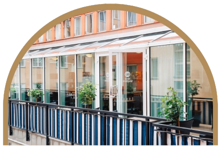 Bilden visar Kom Hotels uteservering som ligger på en innergård mellan husen i Vasastan. Balkongen är inklädd av ett snyggt randigt tyg som ger en modern touch. Här kan man avnjuta en frukost vid caféborden. 