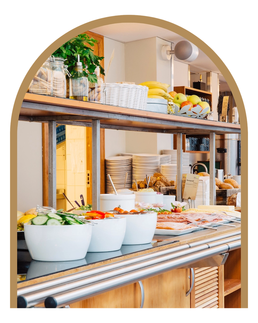 Frukostbuffébord i trä på Kom Hotel. Bordet är överfyllt av en uppdukad frukostbuffé med grönsaker, frukt och pålägg till smörgåsar.