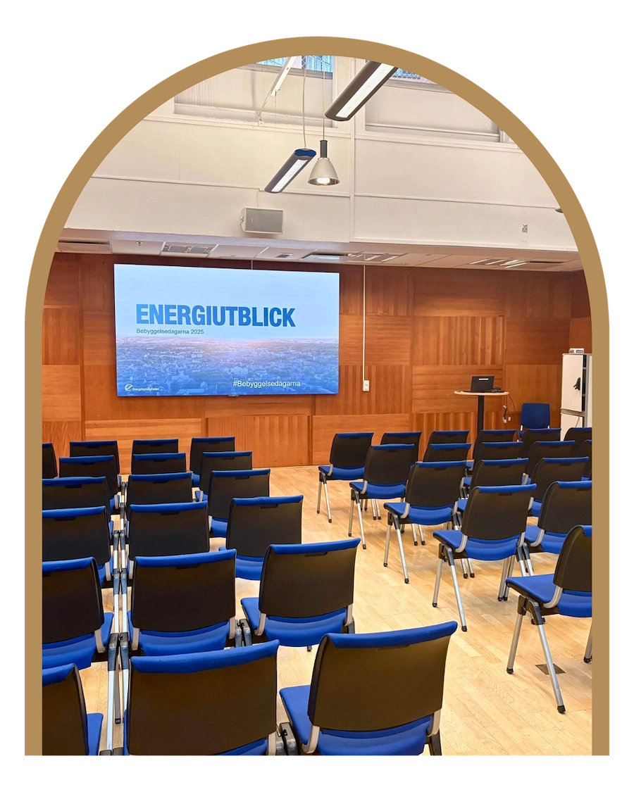 Bilden visar ett konferensrum med en stor skärm som de blå stolarna står vända mot