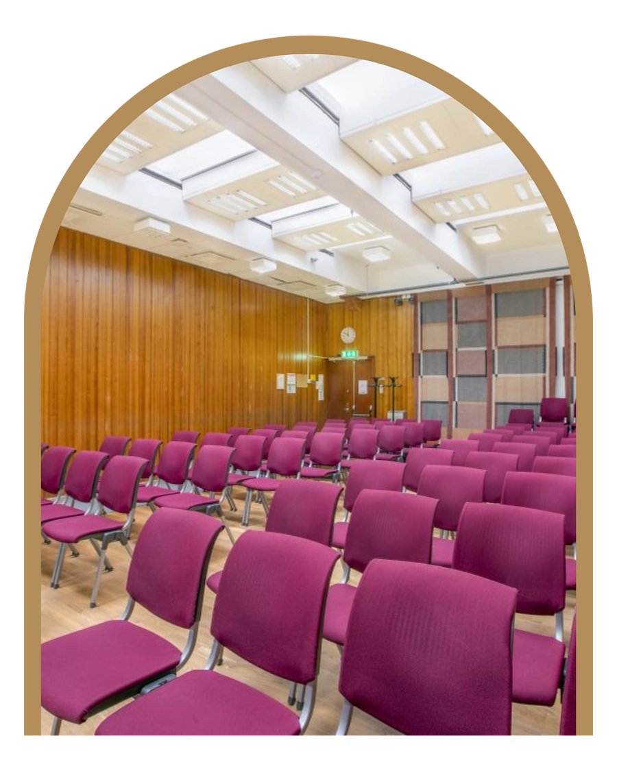 Bilden visar ett konferensrum med cerisa stolar som står vända mot en förmodad scen eller ett podium