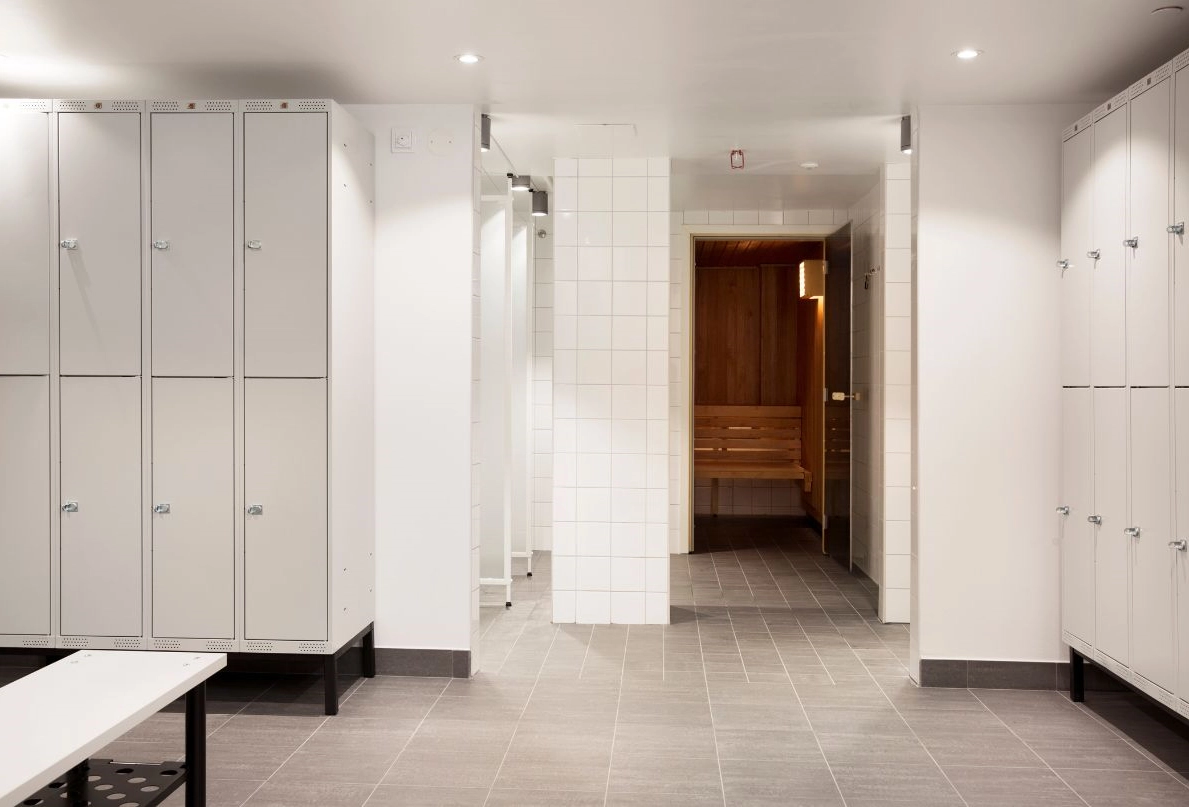 På bilden syns omklädningsrummet som leder till Kom Hotels hotellgym. I omklädningsrummet syns skåp, en bänk och en bastu.