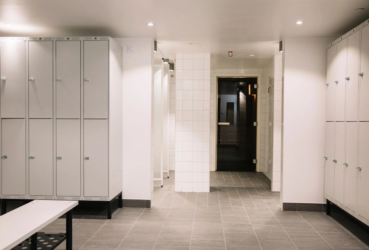 På bilden syns omklädningsrummet som leder till Kom Hotels hotellgym. I omklädningsrummet syns skåp, en bänk och en bastu.