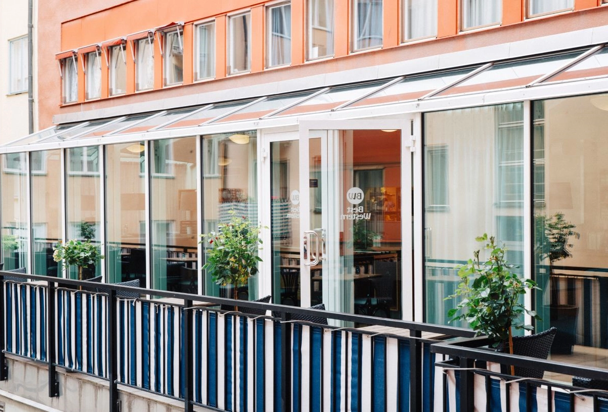 Bilden visar Kom Hotels uteservering som ligger på en innergård mellan husen i Vasastan. Balkongen är inklädd av ett snyggt randigt tyg som ger en modern touch. Här kan man avnjuta en frukost vid caféborden. 