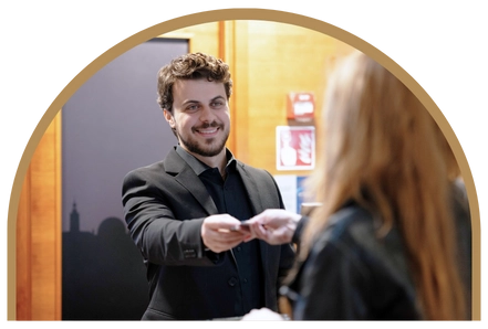 En manlig receptionist på Kom Hotel lämnar leende över ett nyckelkort till en kvinnlig gäst på hotellet.