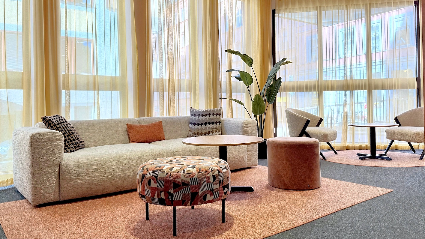 Ett mysig hotellobby med en soffa, fåtöljer, ett soffbord och stora fönster som släpper in mycket ljus.