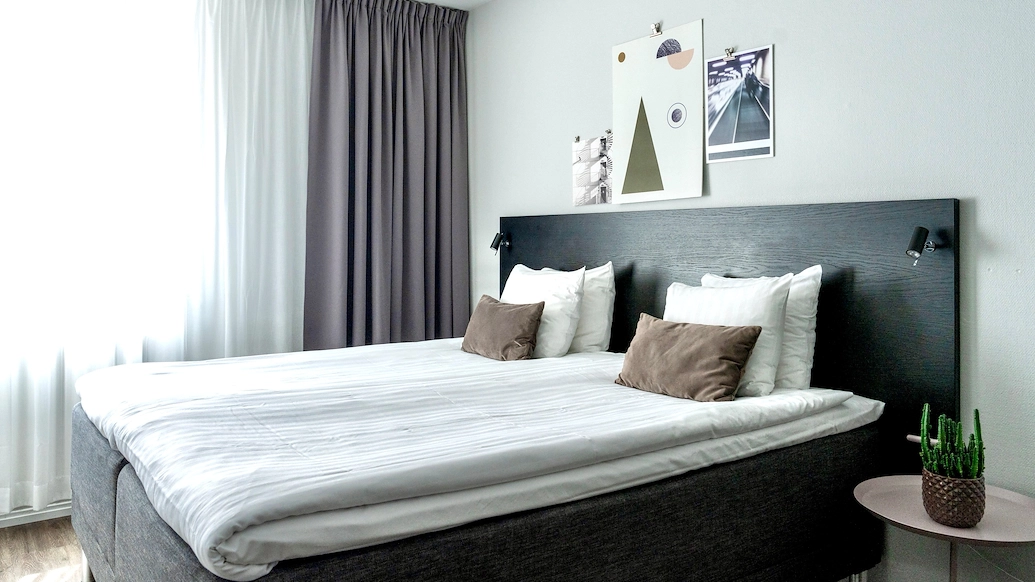 Ett modernt sovrum med en dubbelsäng bäddad med vita lakan och kuddar, Texten "Våra rum" syns i bilden.